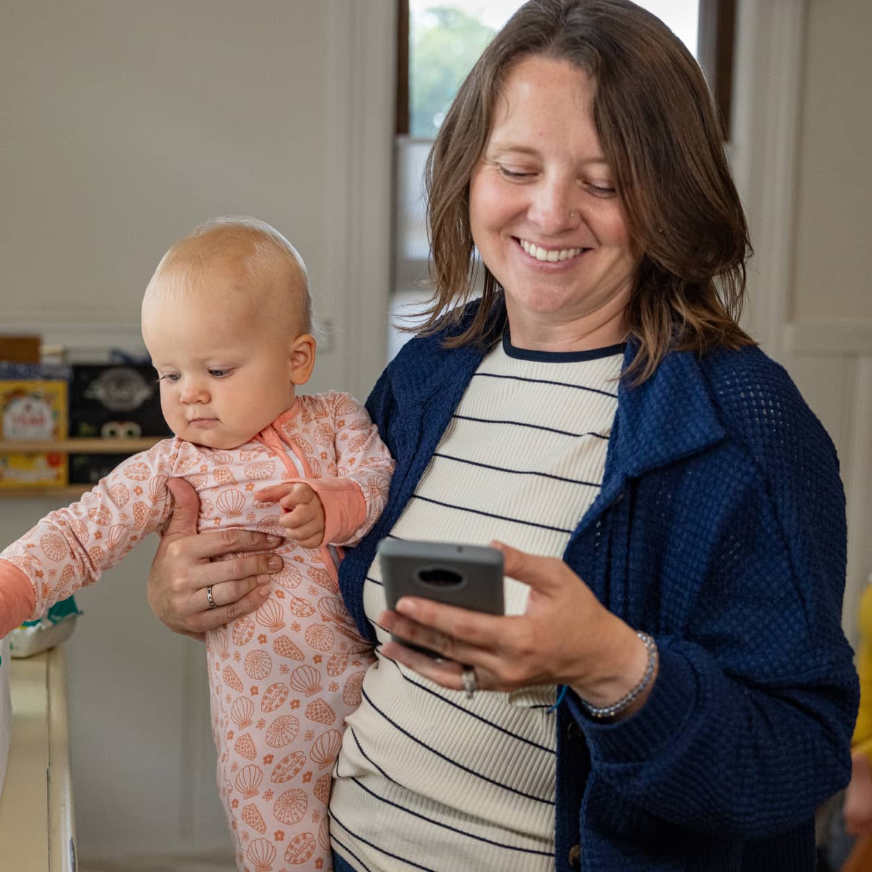 A parent holding a baby with one hand and looking at their cell phone in their other hand.
