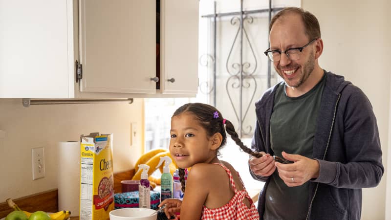 A parent and child in the kitchen at breakfast time.