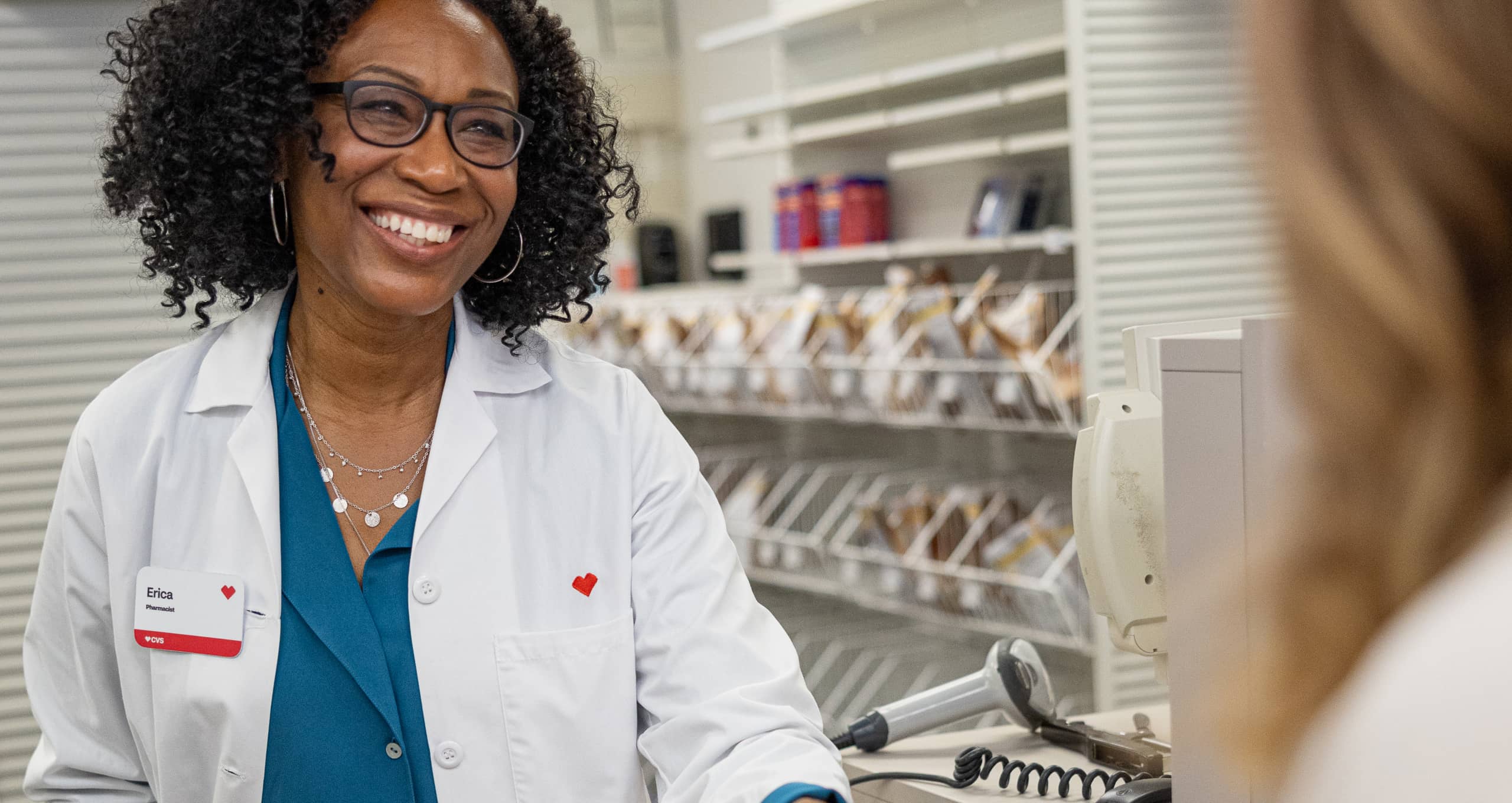 A CVS pharmacist handing a prescription to a customer at the pharmacy counter.